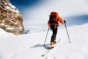 Ski mountaineer climbing up the mountain with a rock on the left