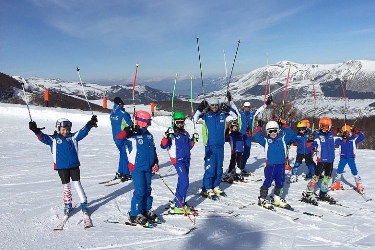 Group of happy kids on a ski slope with their ski poles in the air